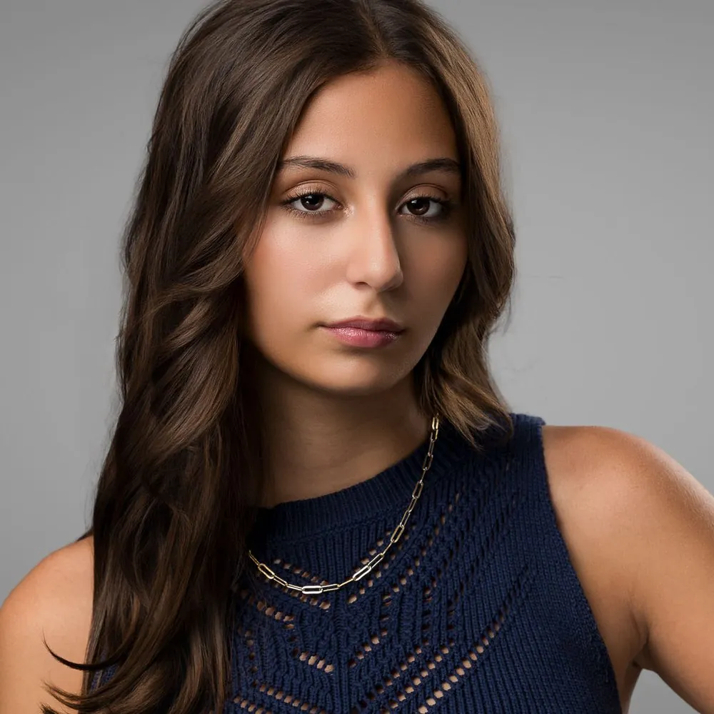 Editorial portrait of a young woman with long brown hair in a navy knit top on a gray backdrop