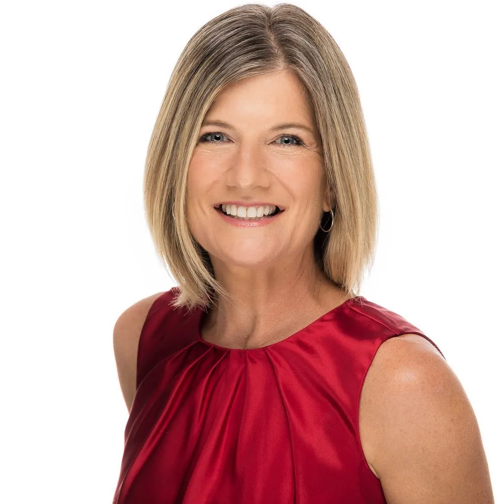 Professional headshot of a woman in a red satin top with a wide smile on a white backdrop